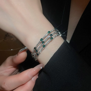 Detail of a three-layer silver bracelet with white crystals and emerald green stones