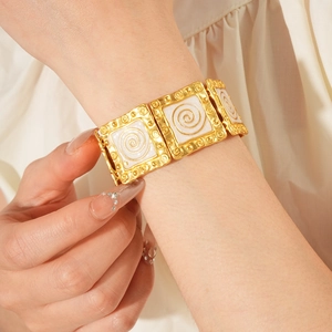 Close-up of vintage golden square bracelet with white enamel spiral patterns on wrist