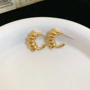 Detailed view of golden twisted C-shaped earrings resting on a white circular dish
