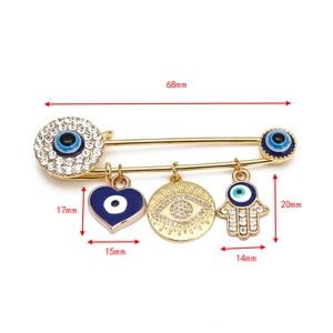 Detail of evil eye safety pin brooch with hamsa hand and heart charms, 68mm length