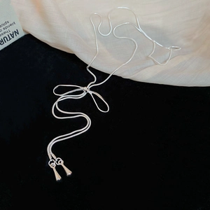 Détail d'un collier nœud argenté avec des pendentifs gouttes d'eau sur un fond en tissu doux