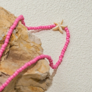 Bohemian style pink bead necklace with beige starfish shell pendant on a natural stone