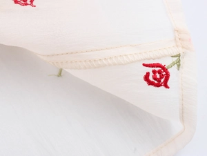 Detail of red floral embroidery on off-white chiffon fabric with rolled hem edges