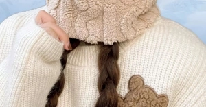 Detailed texture of warm beige plush hood with soft white knit sweater and bear patch