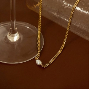 Artistic close-up of a gold chain necklace with a single white pearl on a dark background