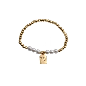 Detailed close-up of gold beaded bracelet with white pearls and letter W charm