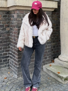 Detail of a white faux fur jacket styled with a pink cap and black wide-leg jeans