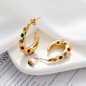 Gold-plated C-shaped earrings with colorful enamel accents on a white ceramic plate