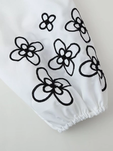 Close-up of white long sleeve with black floral embroidery and elastic cuff details