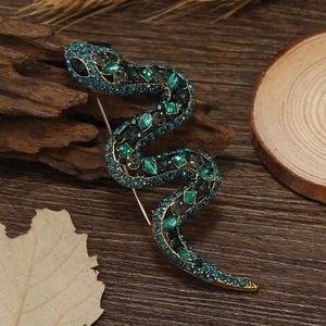 Macro detail of a vintage snake brooch with blue and emerald rhinestones on a wood branch