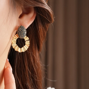 Close-up of model wearing gold hoop earrings with blue rhinestones and textured metal design