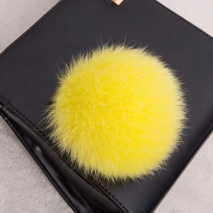 Détail d'un pompon en fourrure jaune vif sur la surface d'un sac à main en cuir noir
