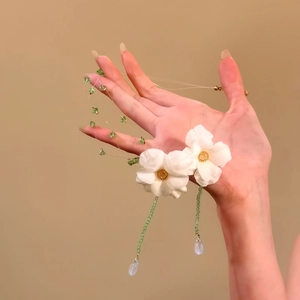 Dettaglio di una collana con fiori in tessuto bianco, perline verdi e pendenti a goccia d'acqua