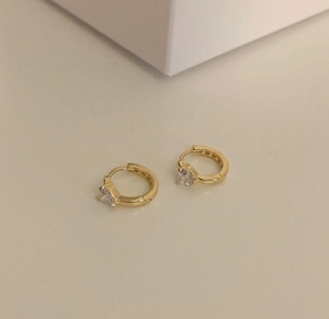 Detailed close-up of golden heart-shaped hoop earrings with sparkling zircon crystals