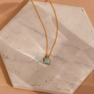 Detail of square gold necklace with blue opal pendant on white marble tray