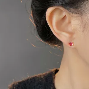 Elegant gold four-prong stud earring featuring a vibrant red square gemstone on ear