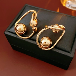 Macro shot of twisted golden metal stud earrings with central sphere on black jewelry box