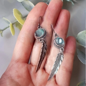 Detail of vintage silver feather earrings with turquoise stone in a hand-held display