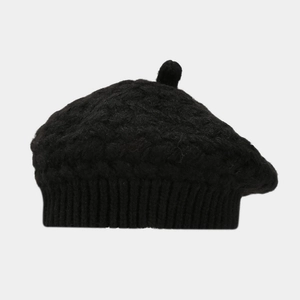 Close-up of black cable-knit wool beret with rib-knit edge and top pompom detail