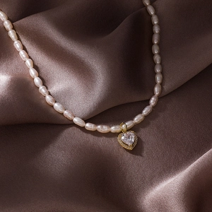 Vue macro d'un collier de perles baroques avec pendentif cœur doré et zircon sur soie