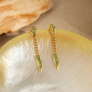 Detail of gold snake earrings with green zircon stones on shell and wood