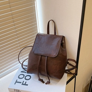 Vintage brown leather backpack with drawstring closure shown on a white book