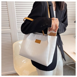 Detailed view of white quilted tote bag with yellow straps worn by model in office setting