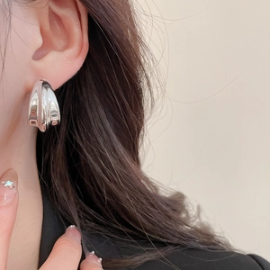 Close-up of model wearing wide silver twist hoop earrings with polished mirror finish
