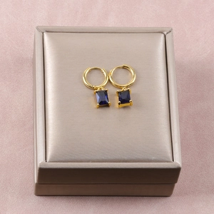 Detalle de pendientes de aro dorados con colgantes rectangulares de gema azul en caja