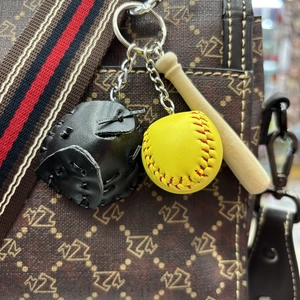 Detail of mini baseball bat, glove and ball keychain hanging on a stylish handbag strap