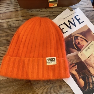 Detail of a bright orange knitted beanie with 1982 label on a rustic wooden surface