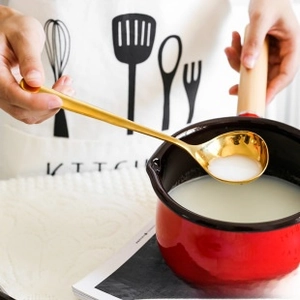 Close-up of golden stainless steel spoon serving porridge from a red enamel pot