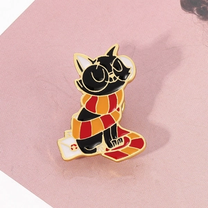 Close-up of a black cat enamel pin wearing a red and orange striped wizard scarf