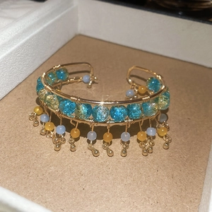 Détail d'un bracelet doré fait main avec perles turquoise et pompons suspendus