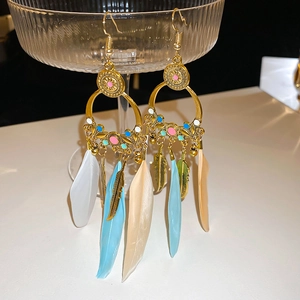 Detailed close-up of Bohemian feather tassel earrings with blue enamel on glass stand