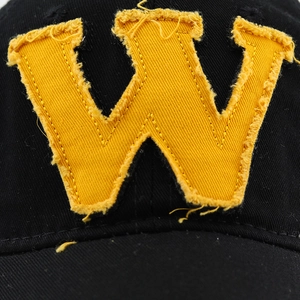Détail de l'écusson W jaune avec bords effilochés sur une casquette en coton noir