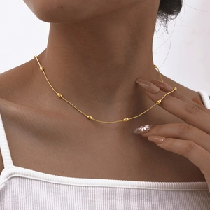 Detailed view of a gold beaded snake chain necklace worn on a woman's collarbone