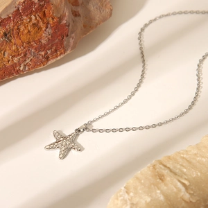 Silver stainless steel starfish pendant necklace with textured surface on white rock