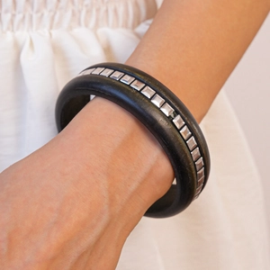Gros plan sur un bracelet en bois noir mat orné de clous carrés en métal argenté de style vintage