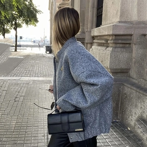 Detail shot of grey tweed loose jacket texture with a black leather handbag style