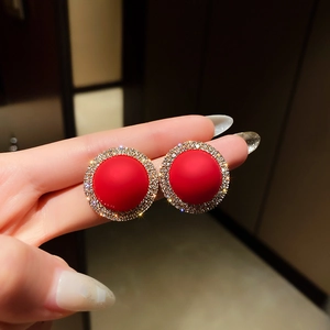 Close-up of red frosted gemstone earrings with a sparkling diamond halo and gold base