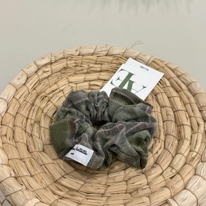 Detailed view of a dark green plaid scrunchie with brand label on a woven basket