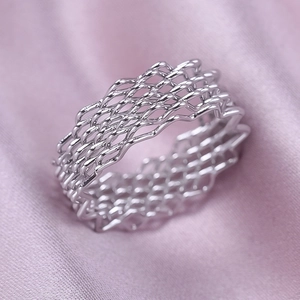 Macro shot of a silver mesh ring featuring layered hollow textures on purple silk fabric