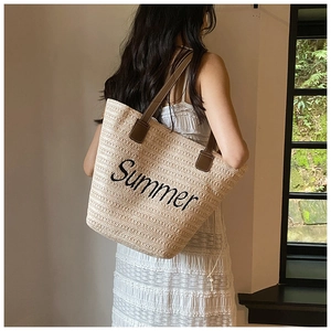 Detail of straw tote bag with Summer embroidery and brown straps on a model