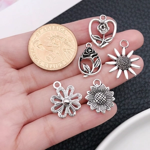 Cinque ciondoli a fiore in argento antico con girasole e rosa accanto a una moneta