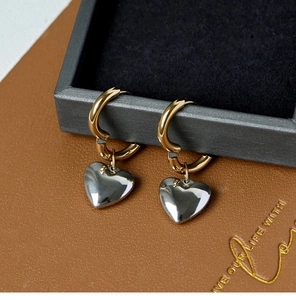 Detailed close-up of heart charm earrings in polished gold and silver finishes