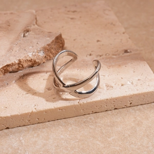 Close-up of a minimalist silver X-shaped criss-cross open ring on a stone pedestal