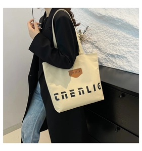 Detailed view of the beige canvas tote bag featuring premium leather logo patch details