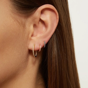 Detail of three gold hoop earrings with white and blue zircons on a female model's ear