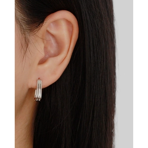 Close-up of minimalist triple-layer silver hoop earrings worn on a female earlobe